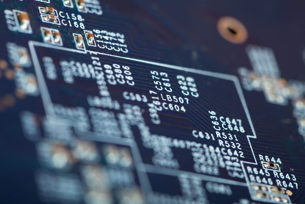 Bližnji posnetek elektronskega tiskanega vezja z opisanimi elektronskimi komponentami, ki ponazarja kompleksnost arhitekture kode in varnostnih protokolov v IT-sistemih.